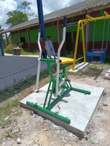 เครื่องออกกำลังกายกลางแจ้งบนแท่นฐานคอนกรีตข้างอาคารชุมชน