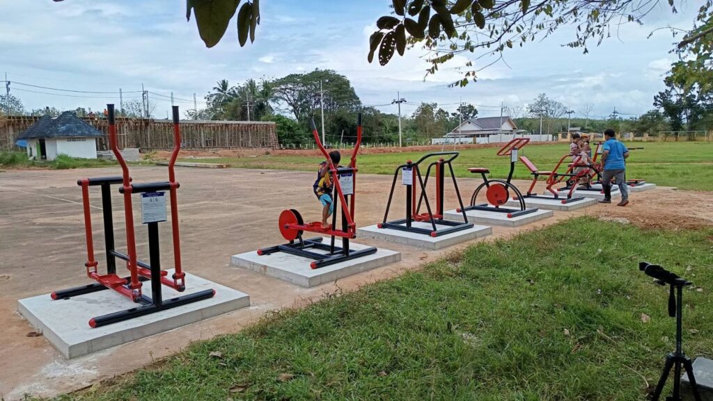 แถวเครื่องออกกำลังกายกลางแจ้งโครงเหล็กสีแดง-ดำ บนแท่นฐานคอนกรีต เทศบาลตำบลปริก